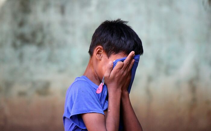 A young boy with his face covered by his hands, conveying sadness or distress related to being a horrible parent.