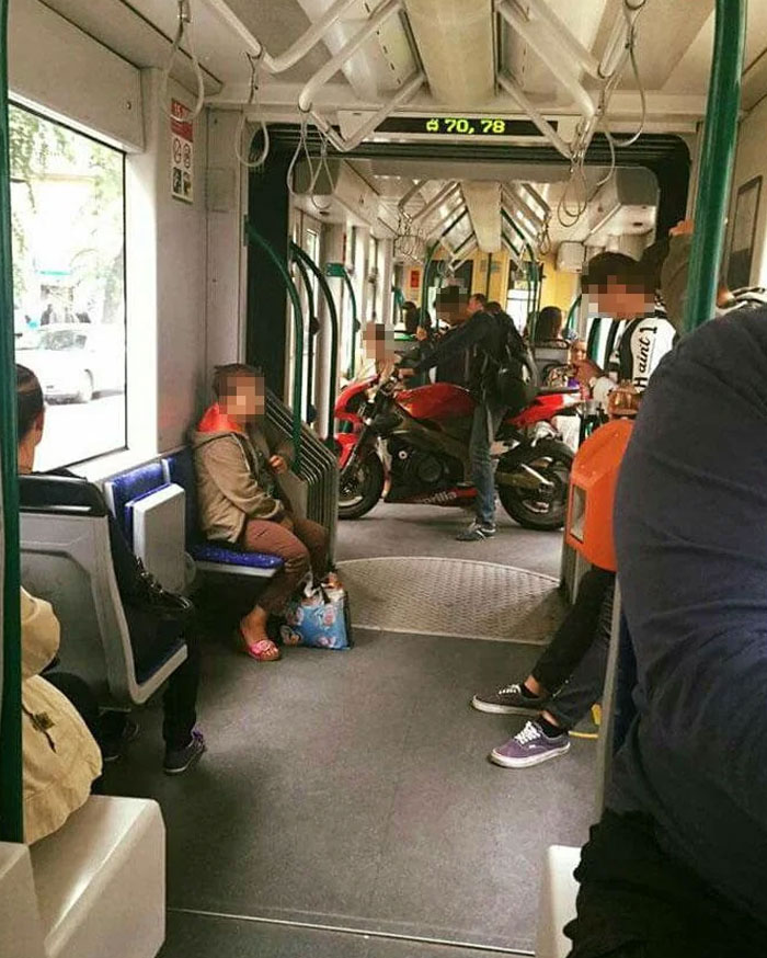 An entitled person on a train with a large red motorcycle, showing entitled folks acting like others are extras.
