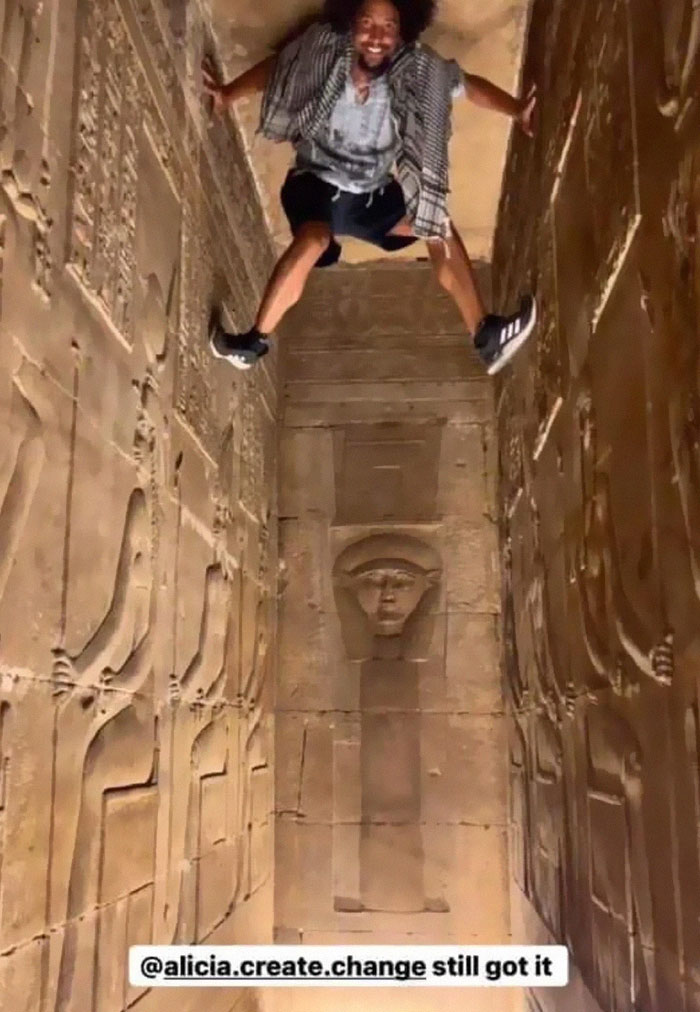 An entitled man poses dramatically, high up on an ancient wall, acting like an extra in his world.