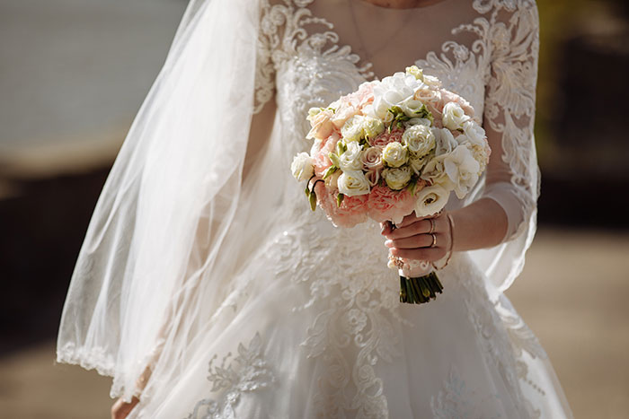 A close-up of a bride in a wedding dress holding a bridal bouquet, showcasing the details of her attire.