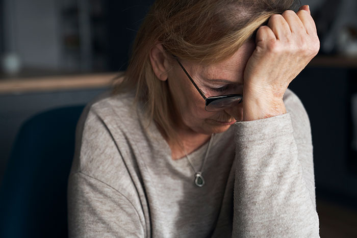 An elderly woman with eyeglasses looks distressed, reflecting the frustration caused by entitled individuals.