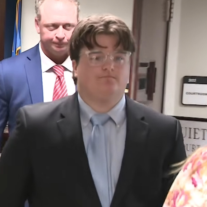 An Oklahoma teen in glasses and a suit, with a serious expression, walking in a courtroom. Facing a prison sentence for brutal crimes.