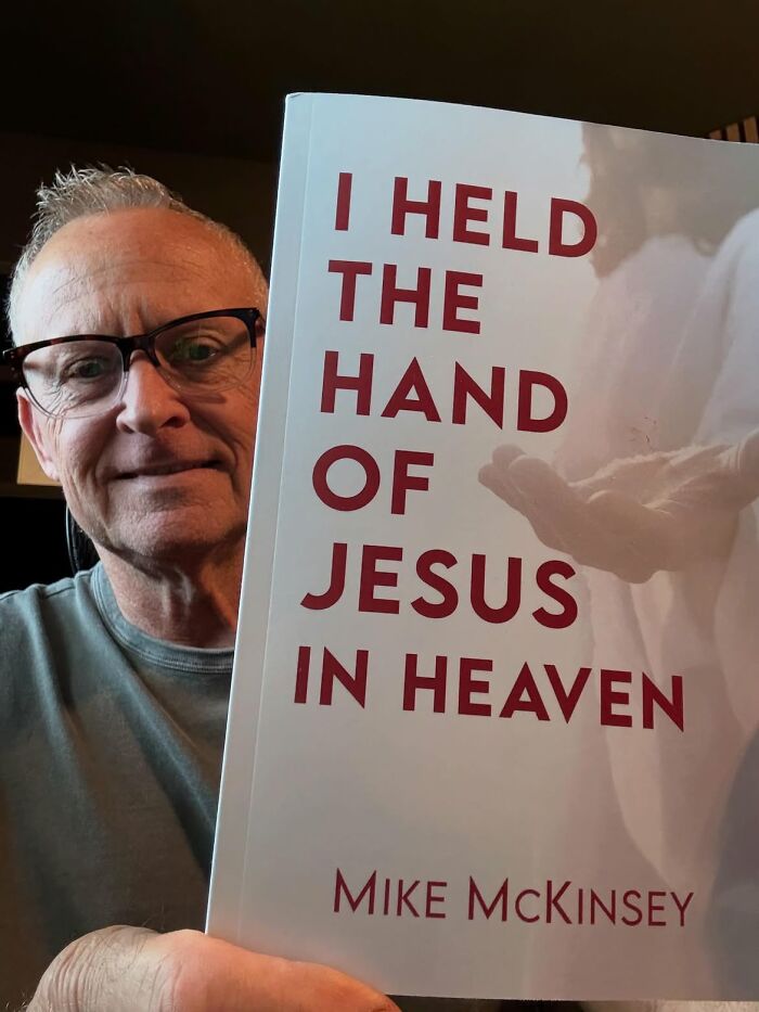 Man holds a book titled I Held the Hand of Jesus in Heaven, detailing his description of the afterlife. Man holds a book titled I Held the Hand of Jesus in Heaven, detailing his description of the afterlife.