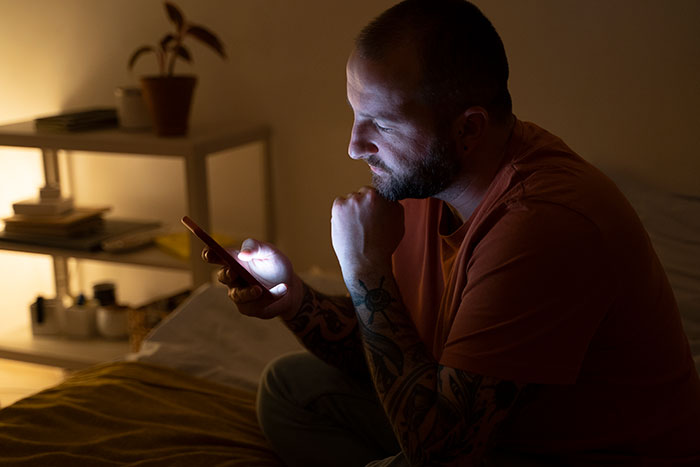 Man looking at his phone in a dimly lit room, turning around and walking out of a party.