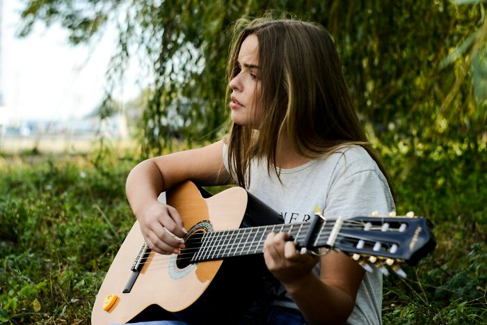 Young woman playing guitar outdoors, reflecting on what dating a celebrity is like.