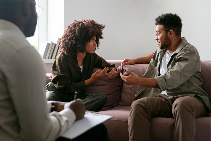 A couple in couples therapy, discussing issues while a therapist takes notes, illustrating a guy mourning his marriage.