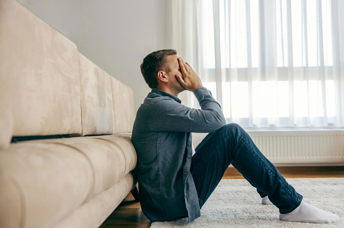 A man sits on the floor, head in hands, looking distraught as he mourns his marriage.