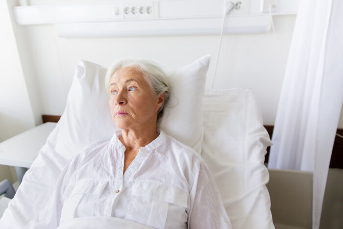 An elderly woman lying in a hospital bed, looking off into the distance, a MIL image.