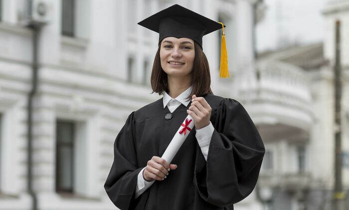A smiling graduate in a cap and gown, holding a diploma, a real deal of her hard work and a sign from the universe.