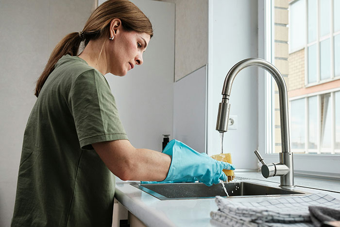 A woman is washing dishes, demonstrating the physical manifestation of the mental load in relationships. A woman is washing dishes, demonstrating the physical manifestation of the mental load in relationships.