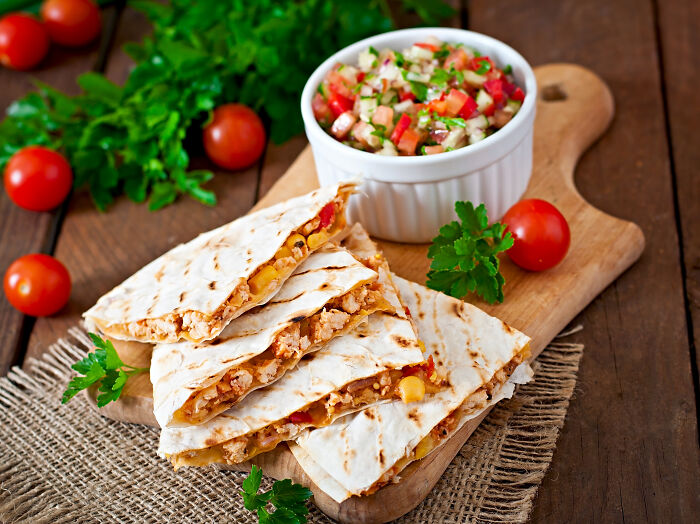 Delicious quesadillas on a wooden board with fresh salsa and tomatoes, representing unhinged house rules about shared food.