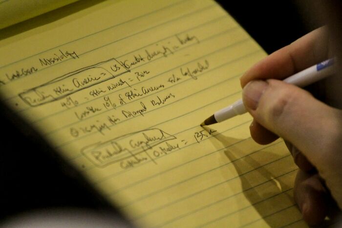 A hand writing notes on a yellow pad, showing the process of picking up a new skill in 30 days.