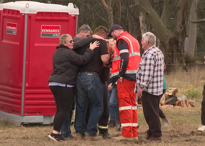 People embracing near a portable toilet, grieving after the tragic finding of the missing teen's body.