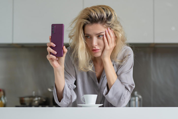 A woman looking at her phone, feeling sad about losing best friends after a bachelorette date dispute. A woman looking at her phone, feeling sad about losing best friends after a bachelorette date dispute.