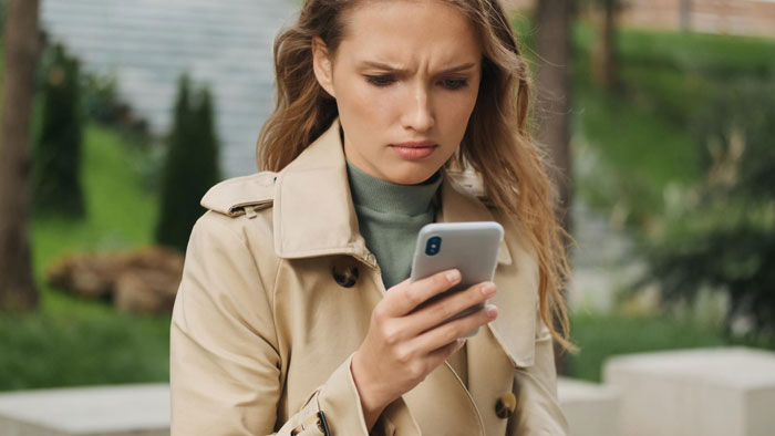 A woman looks confused while checking her phone, reflecting a bachelorette dispute and friendship ending. A woman looks confused while checking her phone, reflecting a bachelorette dispute and friendship ending.