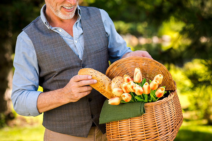 A man with a new bf in a light blue shirt and grey vest, smiling and holding a picnic basket with bread and tulips. A man with a new bf in a light blue shirt and grey vest, smiling and holding a picnic basket with bread and tulips.