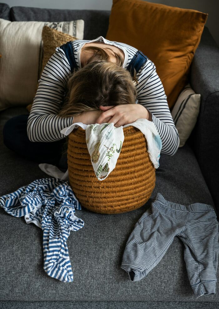 A mother with her head buried in a laundry basket on the couch, exhausted by the struggles of being a parent.