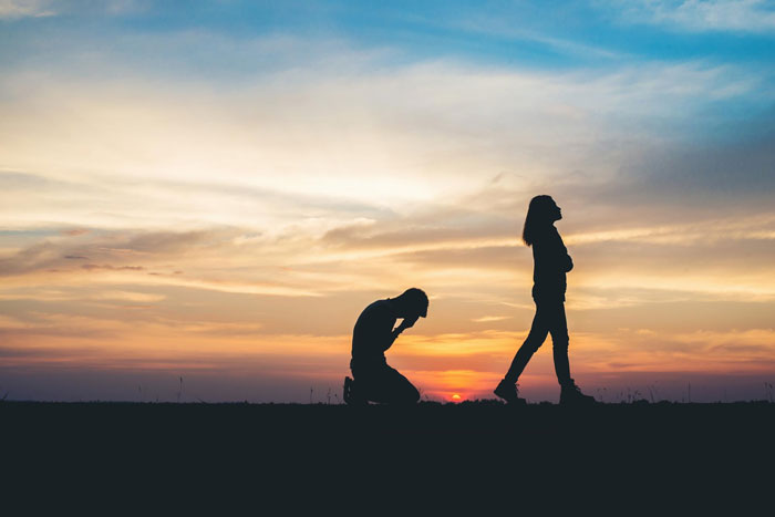 Silhouette of a guy in debt after his cheater wife ditches him, kneeling while she walks away at sunset. Silhouette of a guy in debt after his cheater wife ditches him, kneeling while she walks away at sunset.