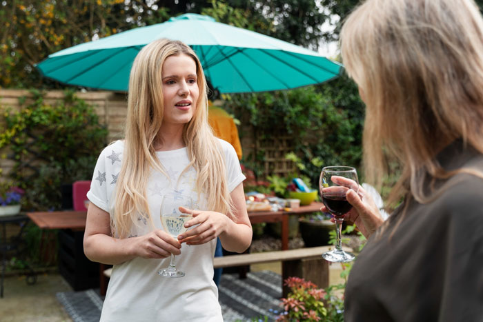 Daughter's surprise graduation BBQ: A young woman holds a drink, talking to an older woman at an outdoor BBQ. Daughter's surprise graduation BBQ: A young woman holds a drink, talking to an older woman at an outdoor BBQ.