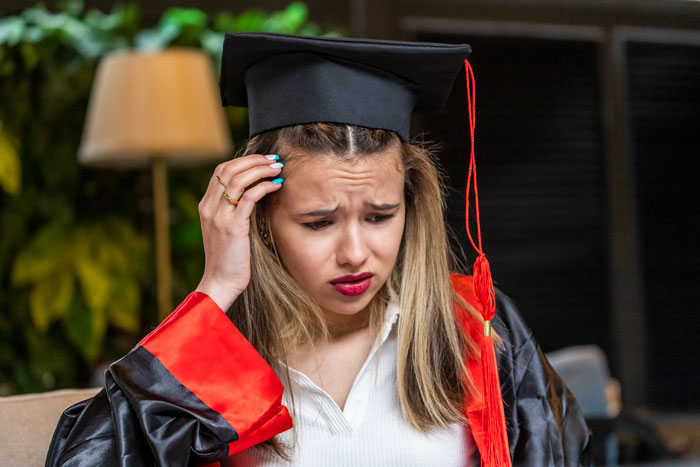 A girl in graduation attire looking upset, reflecting on her graduation BBQ. A girl in graduation attire looking upset, reflecting on her graduation BBQ.