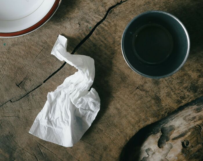 A crumpled tissue and a metal cup on a wooden table, representing a poverty habit of frugality.