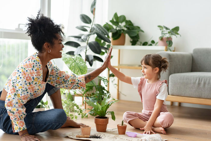 A woman and a young girl high-fiving while potting plants, representing a strong best friend relationship on a family vacation. A woman and a young girl high-fiving while potting plants, representing a strong best friend relationship on a family vacation.