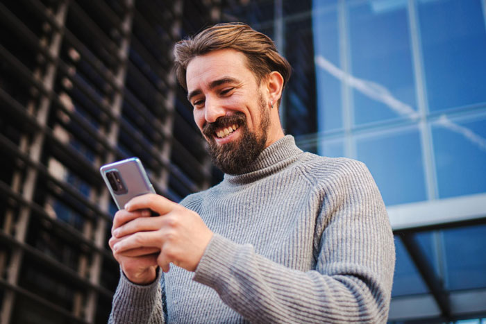 A smiling man looking at his phone, representing the family vacation and in-laws drama. A smiling man looking at his phone, representing the family vacation and in-laws drama.