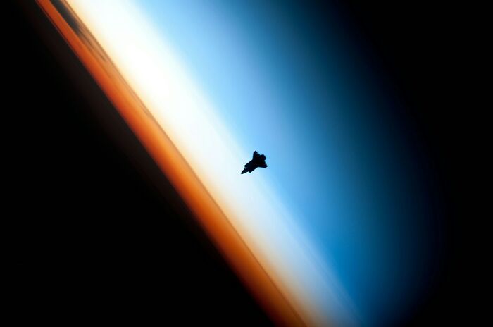 A space shuttle silhouetted against Earth's atmosphere, demonstrating interesting scientific facts about space.
