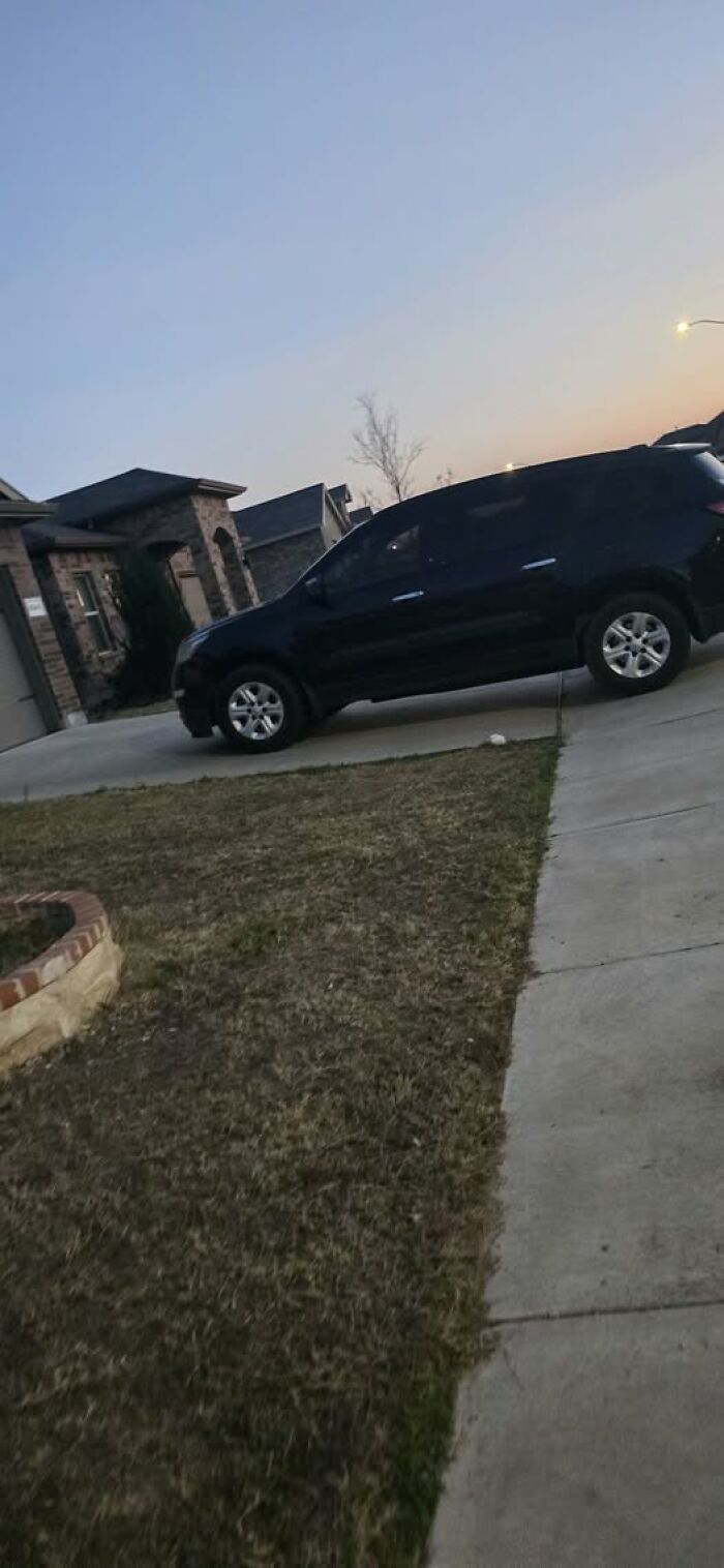 A black SUV parked partially on a driveway and lawn, demonstrating jerk neighbor parking.