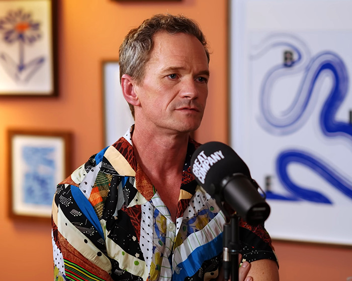 How I Met Your Mother star in a patterned shirt, speaking into a podcast microphone about the controversy.