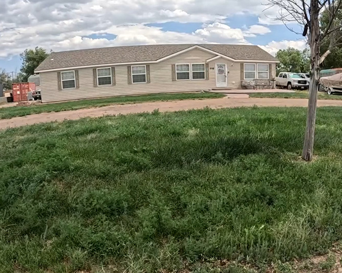 A beige house, the Zillow listing home, with green grass in the foreground and a cloudy sky. A beige house, the Zillow listing home, with green grass in the foreground and a cloudy sky.