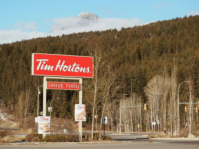 Tim Hortons drive-through sign with mountains and trees in the background. Shows a drive-through restaurant.