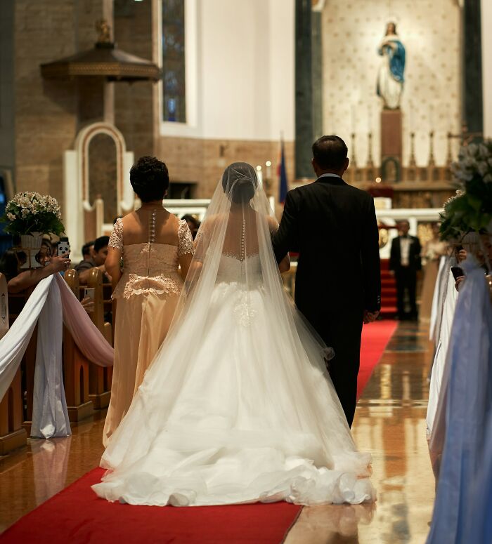 A bride walks down the aisle with her parents, capturing a beautiful wedding moment.