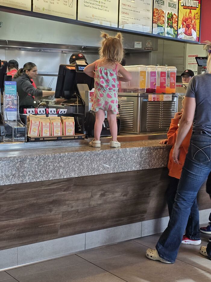 A young child stands on a counter at a restaurant while a parent stands nearby, showing a parenting problem.