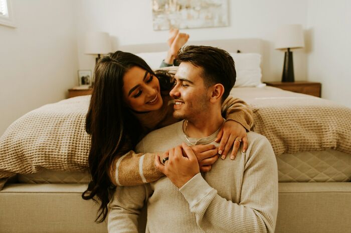 A happy young couple smiling and embracing on the floor next to a bed, representing the truths about being married.