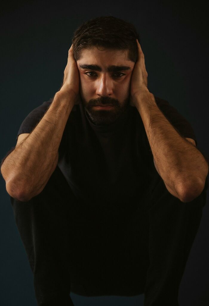 A man with hands over his ears, looking distressed from creepy true stories that question reality.