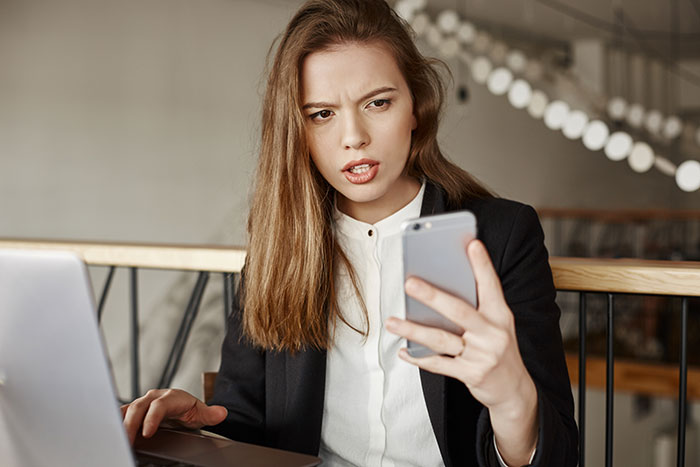 A woman looking frustrated while holding her phone, perhaps reacting to her fiancé's anger after she blocked his card for not cleaning. A woman looking frustrated while holding her phone, perhaps reacting to her fiancé's anger after she blocked his card for not cleaning.