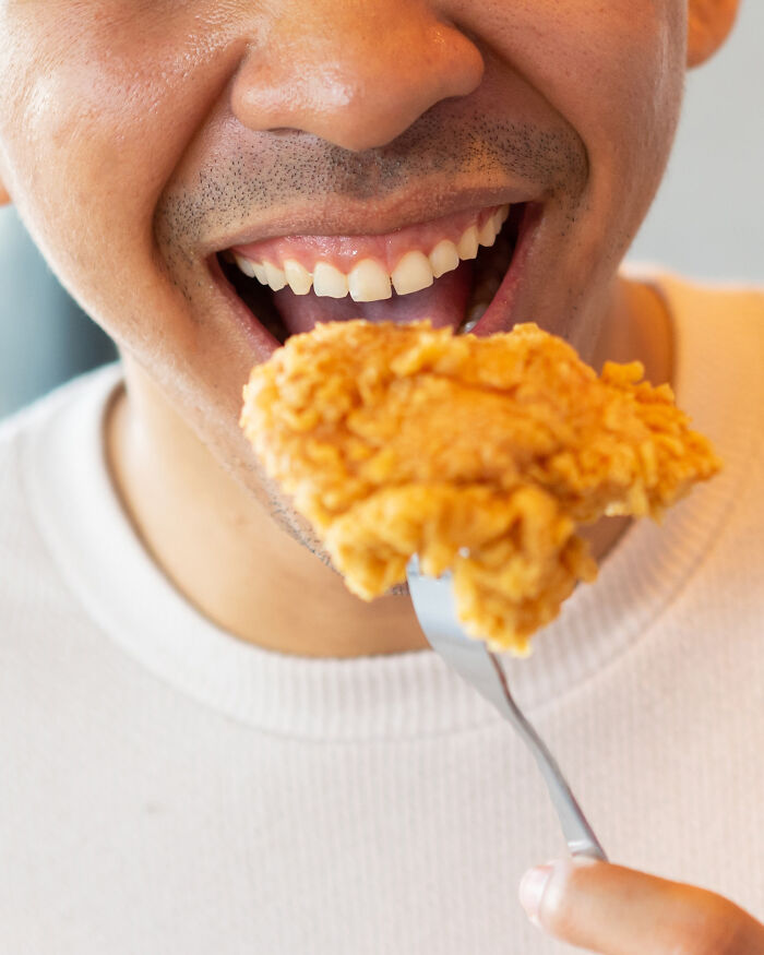 Close-up of a person eating fried chicken with their mouth open, central to the viral debate about plane etiquette.