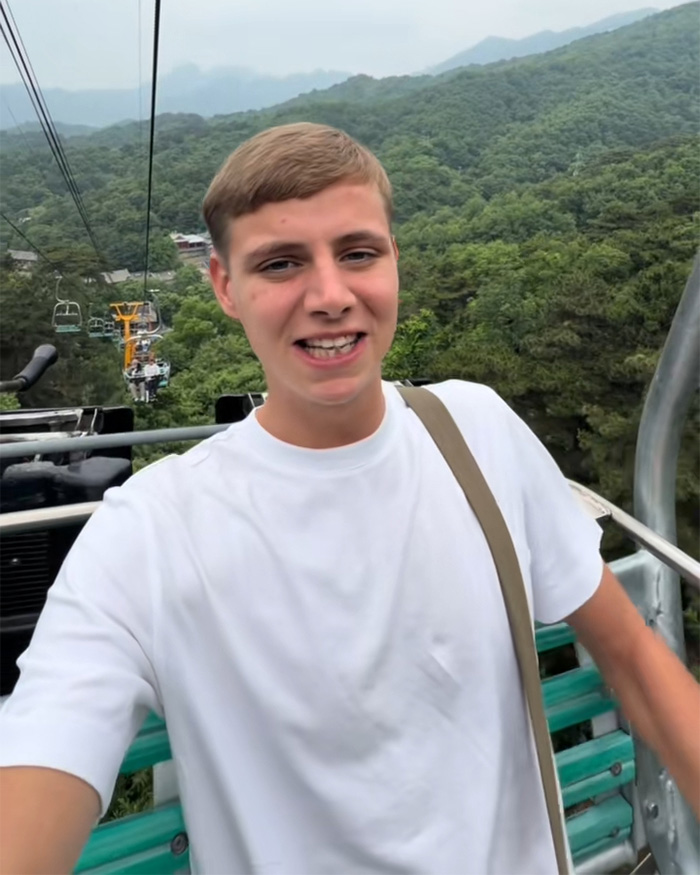 Young man on a chairlift overlooking mountains, smiling towards the camera, part of a viral debate about plane etiquette.