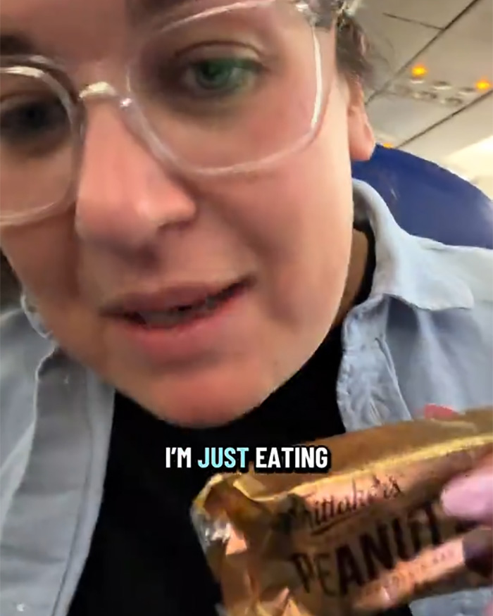 A passenger on a plane holds a peanut bar, explaining she's just eating peanuts on plane. A passenger on a plane holds a peanut bar, explaining she's just eating peanuts on plane.