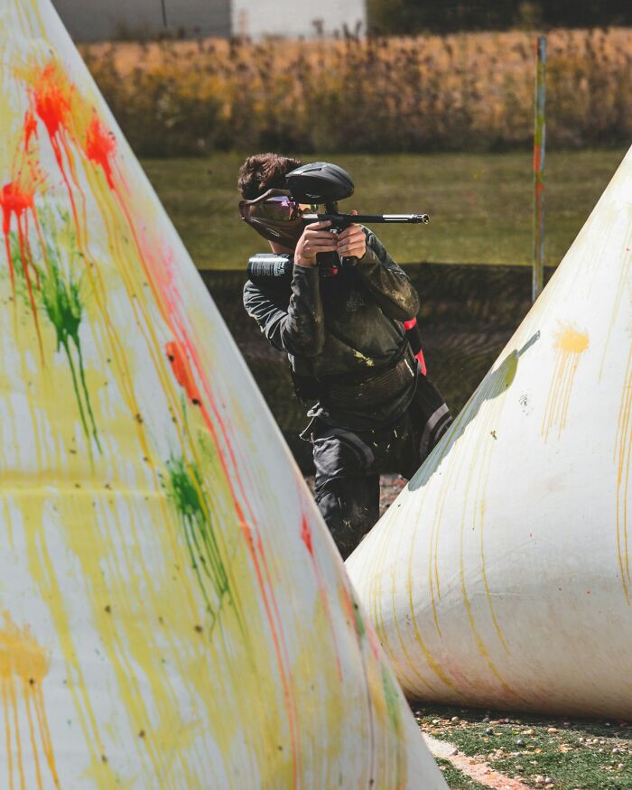A person in paintball gear, covered in paint, playing in a field, showing the freedom of college life activities.
