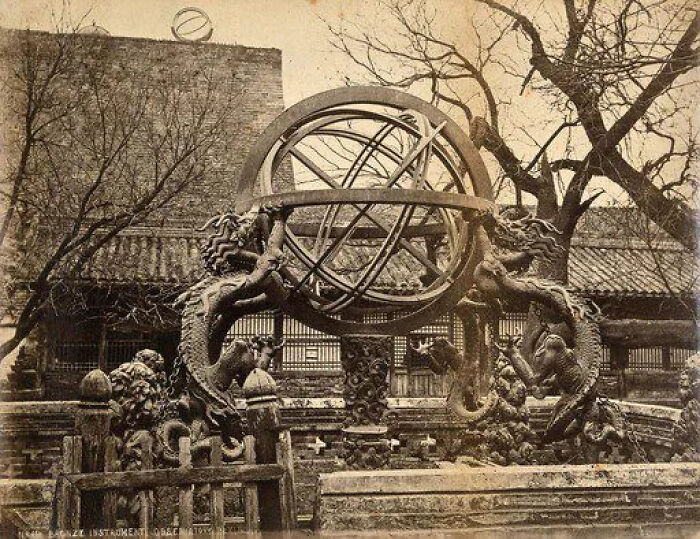Sepia-toned image of an ornate bronze armillary sphere, historical artifact, supported by dragons, against a traditional building.