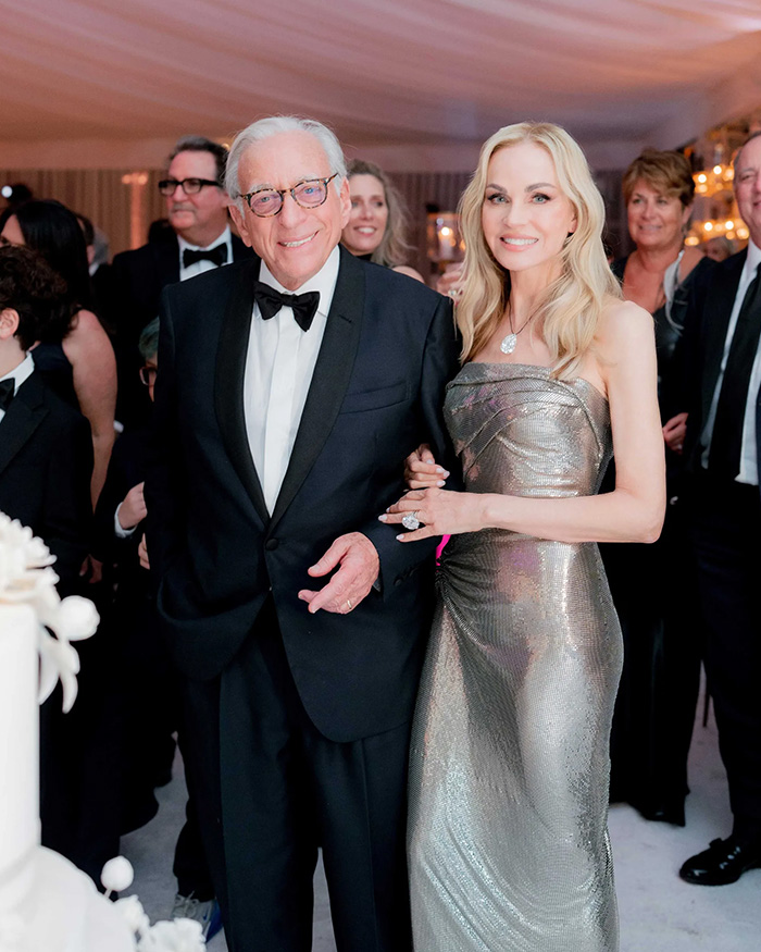A couple smiling at a wedding, with the man in a tuxedo and the woman in a shimmering gown, amidst other wedding guests. A couple smiling at a wedding, with the man in a tuxedo and the woman in a shimmering gown, amidst other wedding guests.
