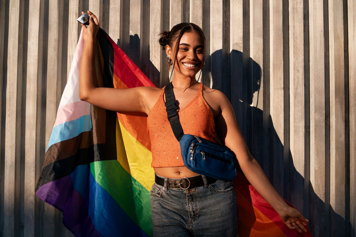 A woman smiling and holding a Progress Pride flag, representing evolving identity and the term Almondsexual. A woman smiling and holding a Progress Pride flag, representing evolving identity and the term Almondsexual.