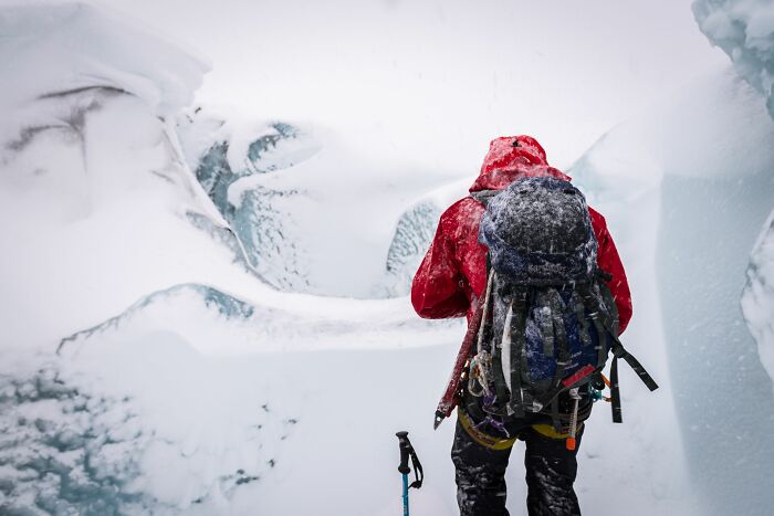 A lone person in red winter gear with a backpack traversing a snowy, icy landscape, a scariest thing to witness.