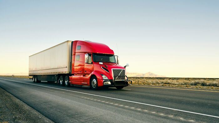 A bright red semi-truck with a white trailer drives down a highway in a desert landscape, symbolizing scary things witnessed.