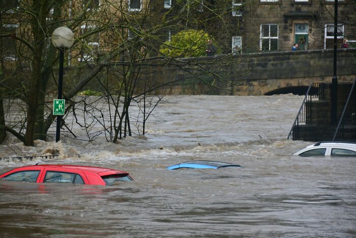 Scariest things witnessed: Several cars are submerged in muddy floodwaters next to a bridge and buildings, showing a natural disaster.