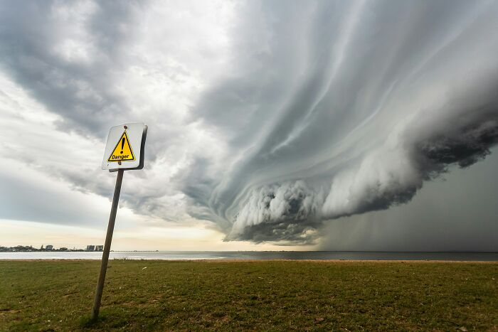Scariest things witnessed: A danger sign stands on a grassy shore as a massive, ominous storm cloud looms over the water.