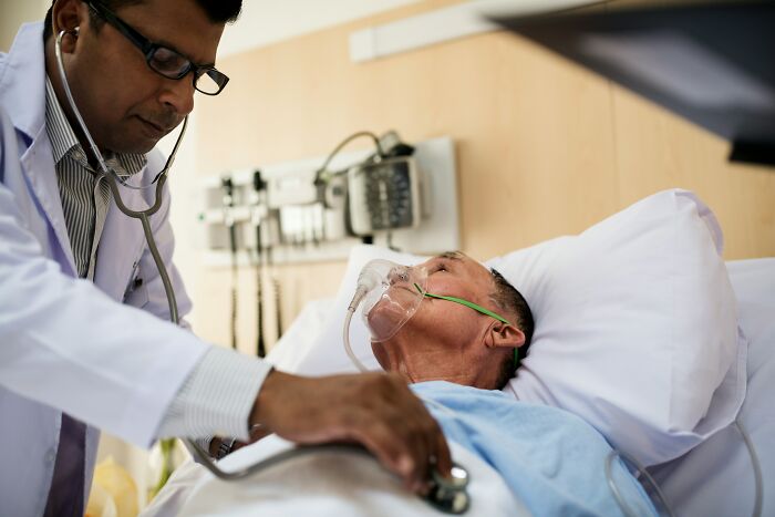 A doctor uses a stethoscope on a patient with an oxygen mask, highlighting scariest things witnessed in a hospital.
