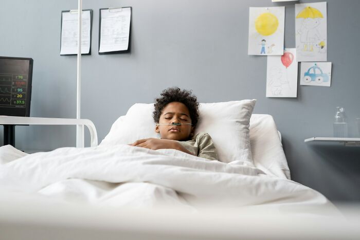 A young child with a nasal cannula sleeps in a hospital bed with drawings on the wall, reflecting scariest things witnessed.